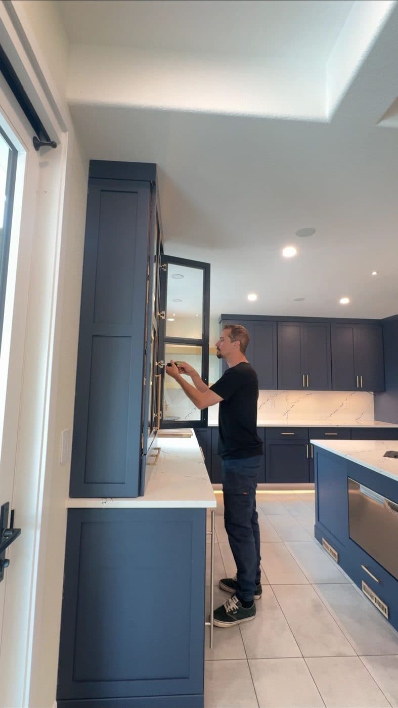 Alex hanging a glass-front cabinet door in a navy kitchen