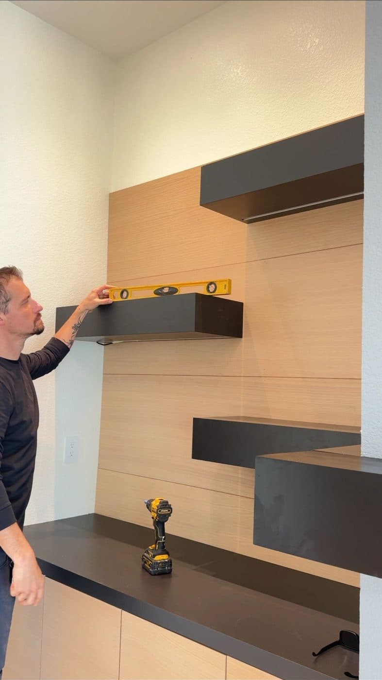Alex leveling a floating shelf on an oak wall