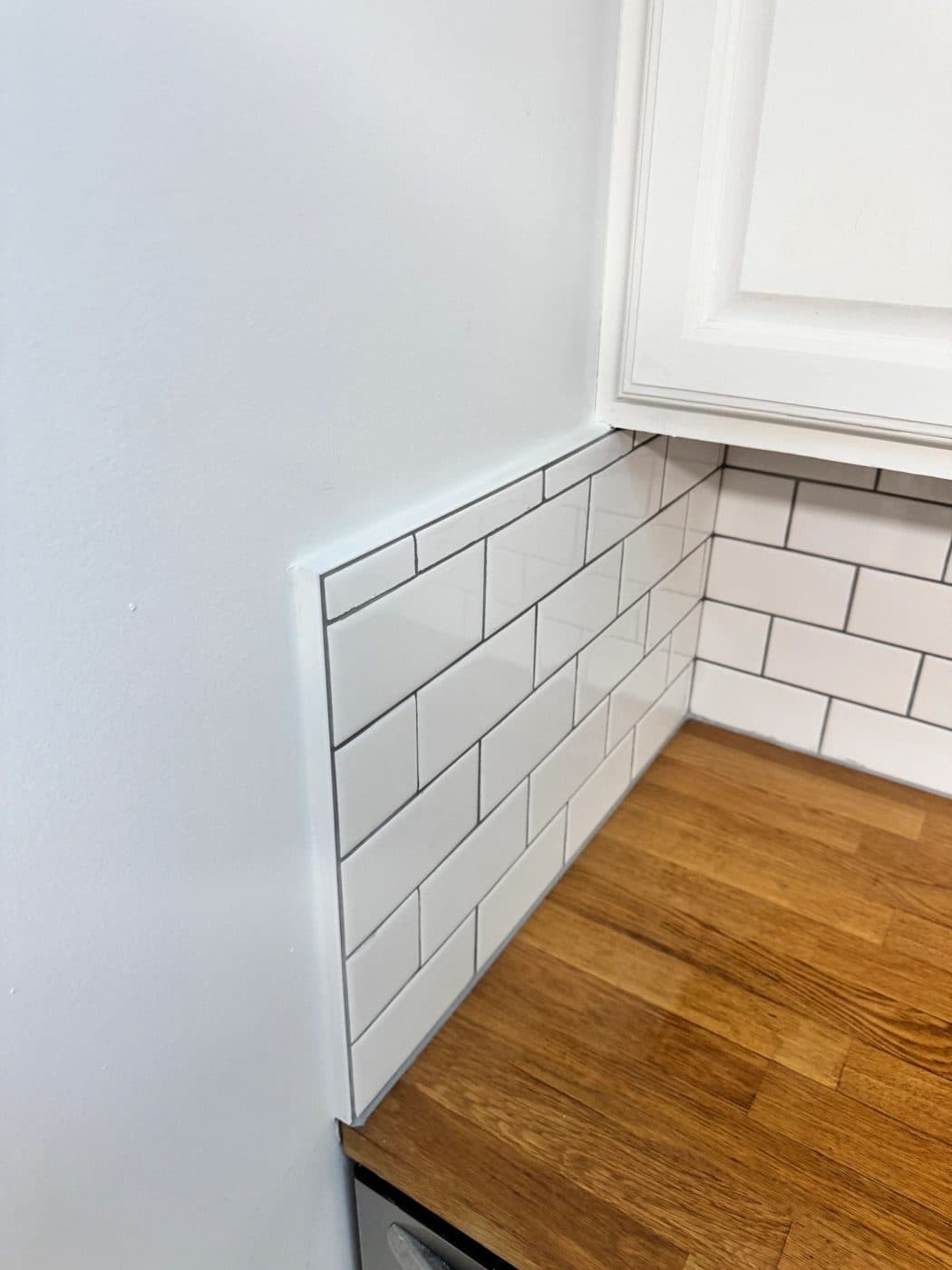 A white subway-tile backsplash in a kitchen corner above a butcher-block counter