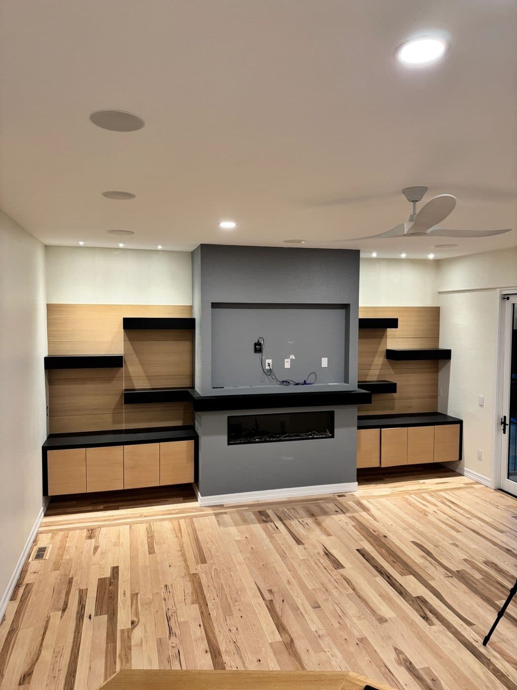 A living room wall with black floating shelves, a floating mantel and a fireplace