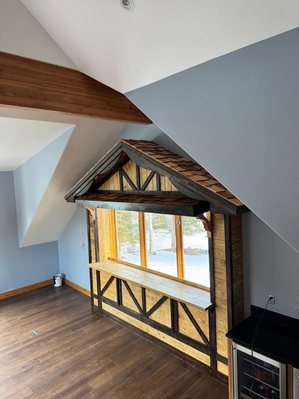 A half-timbered window nook with cedar shingles and a bar ledge in a vaulted room