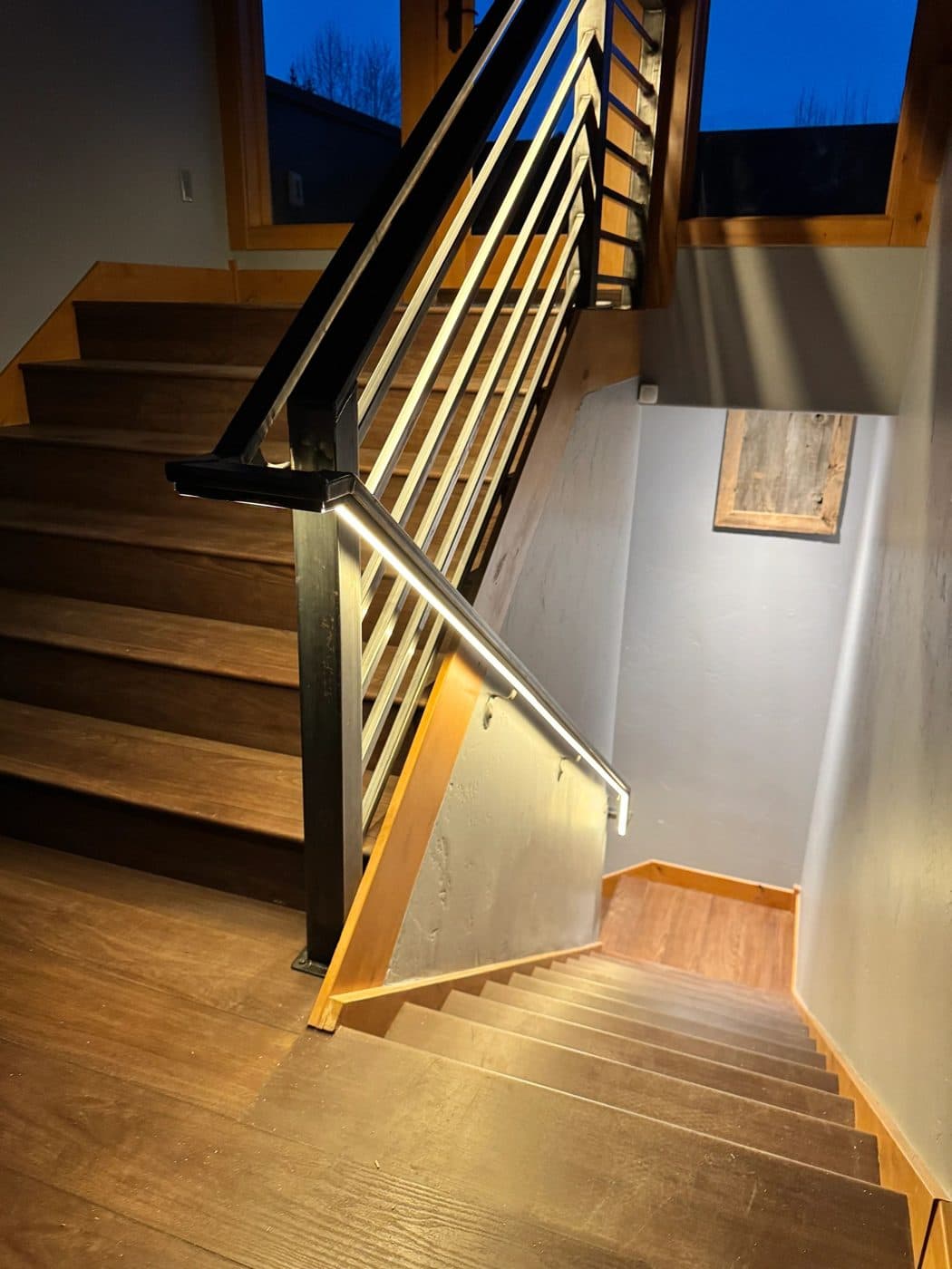 A stairwell with a lit steel handrail above wood treads