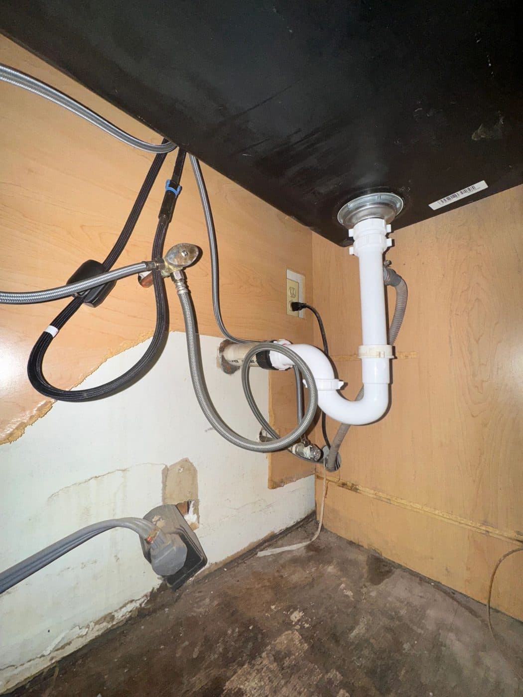 The inside of a sink cabinet showing a drain trap, braided supply lines and shut-off valves